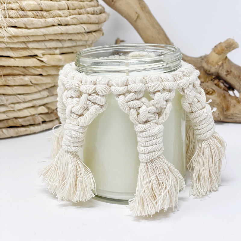 Unlit candle with a macrame cover on it to show what it looks like without the candle lit.  There is driftwood in the background.