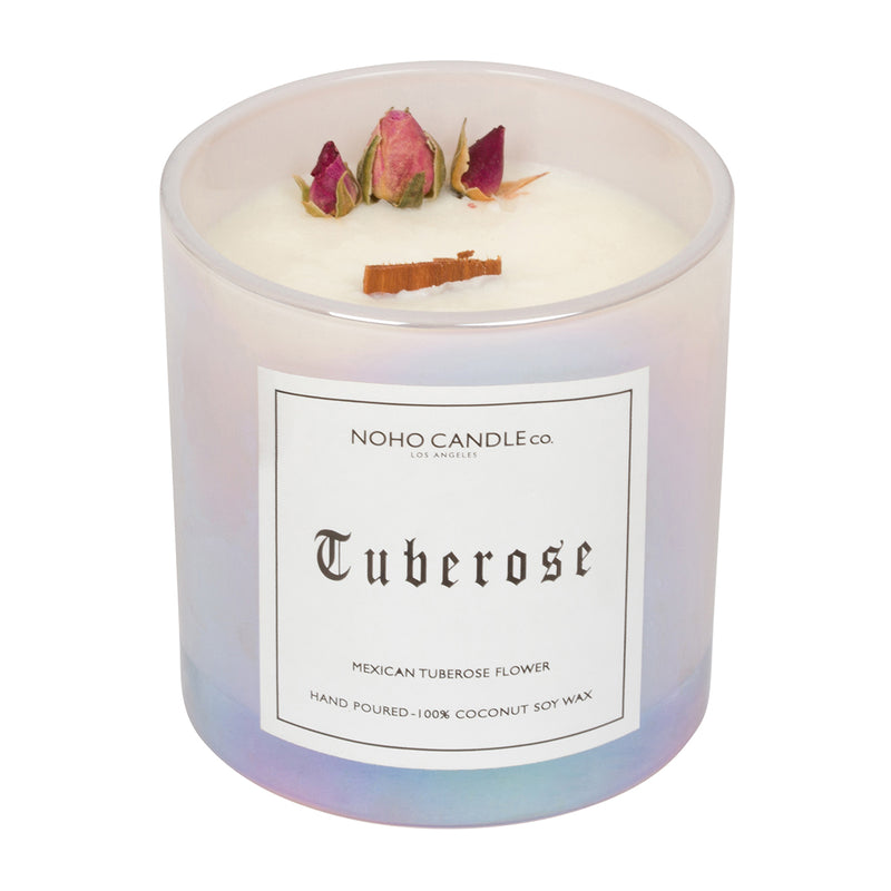 A 10oz wood wick Tuberose floral collection candle.  The wax is white and there are three dried, natural roses arranged artfully near the edge.  The candle has been poured into an iridescent glass that comes with a clear, translucent lid.