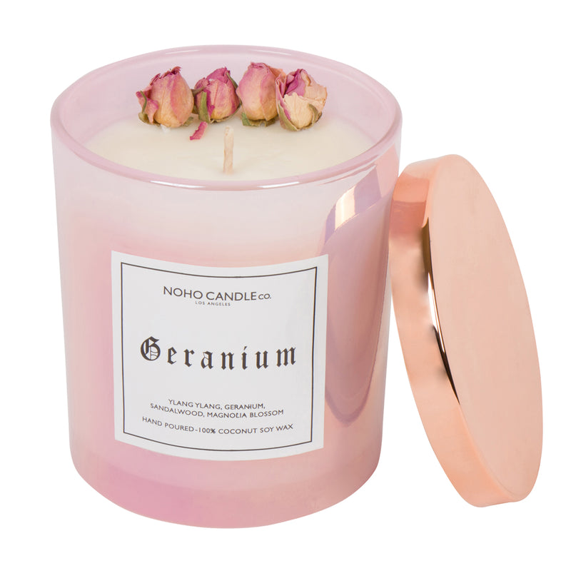 A 14oz cotton wick Geranium floral collection candle.  The wax is white and has four dried, natural roses along the edge. The candle is in a pink iridescent glass with a copper lid that pops off and on.